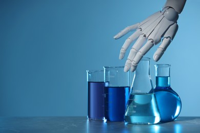 Photo of Artificial intelligence. Robot hand and laboratory glassware with liquids on table against light blue background, space for text