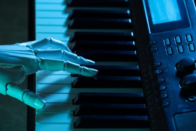 Photo of Artificial intelligence. Robot hand playing synthesizer in blue light, closeup