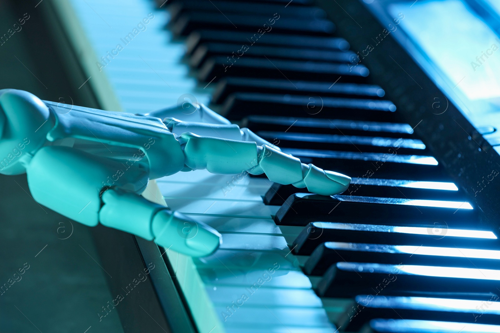 Photo of Artificial intelligence. Robot hand playing synthesizer in blue light, closeup