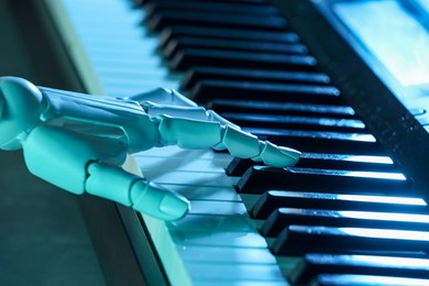 Photo of Artificial intelligence. Robot hand playing synthesizer in blue light, closeup