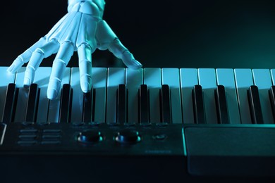 Photo of Artificial intelligence. Robot hand playing synthesizer on dark background in blue light, closeup