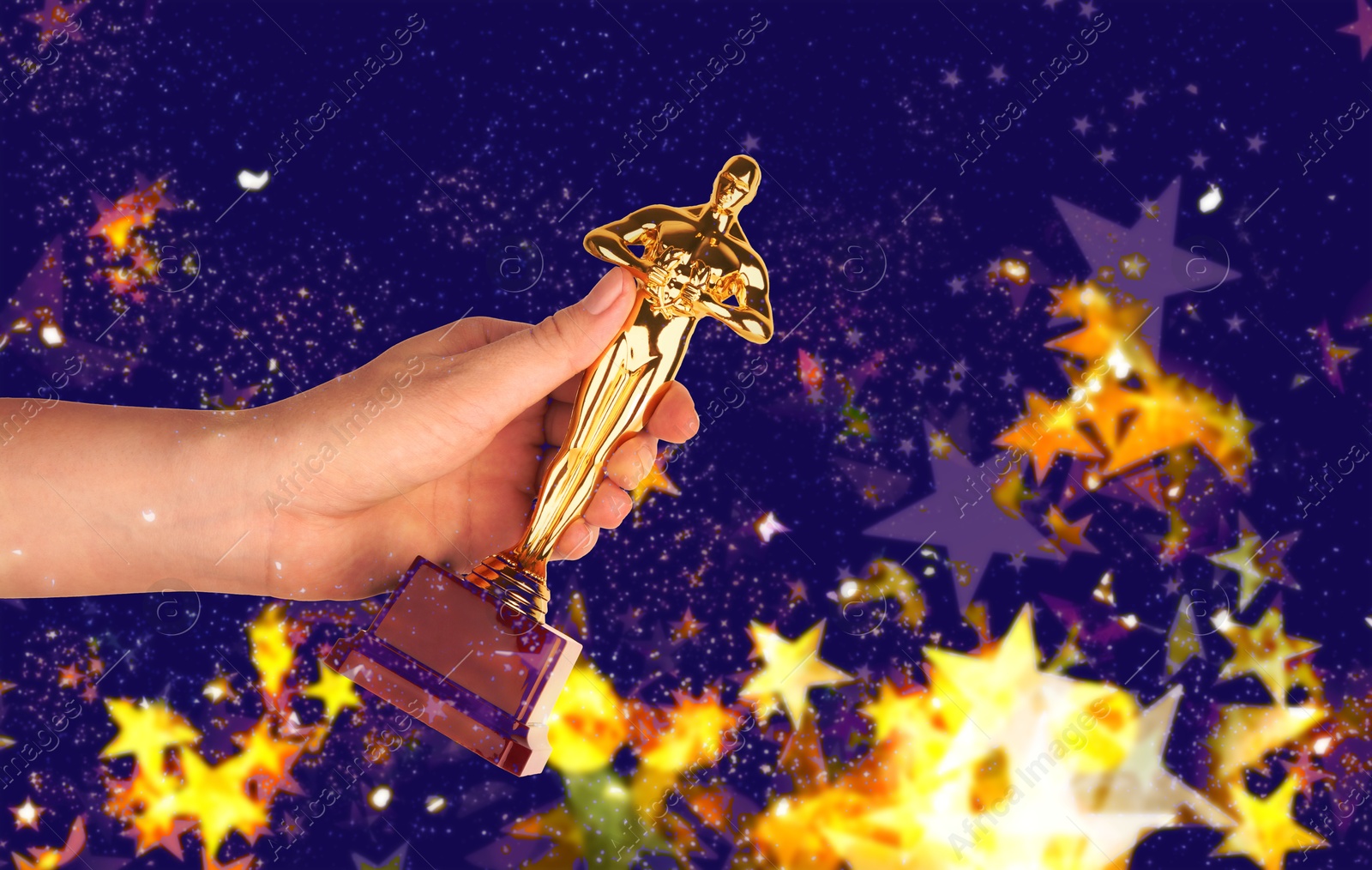 Image of Woman holding golden trophy in shape of human figure on dark background. Shimmering stars and blurred lights