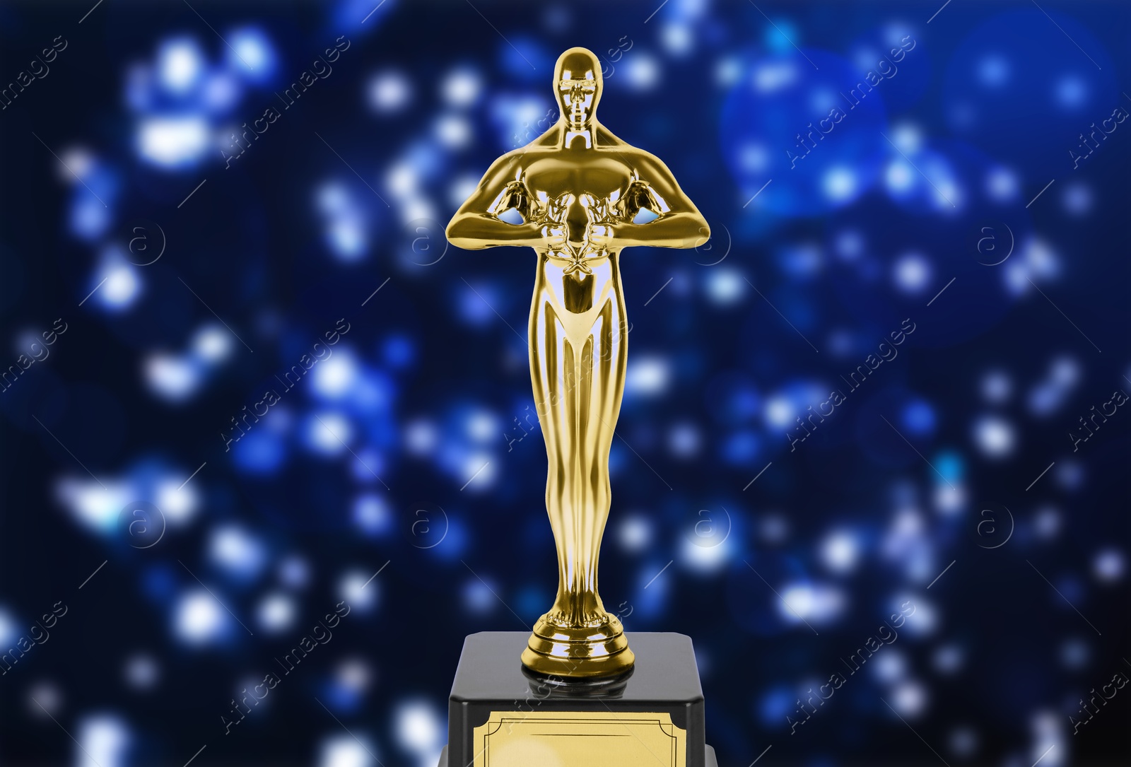 Image of Golden trophy in shape of human figure on dark blue background with blurred lights