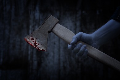 Image of Man holding bloody axe outdoors, closeup view