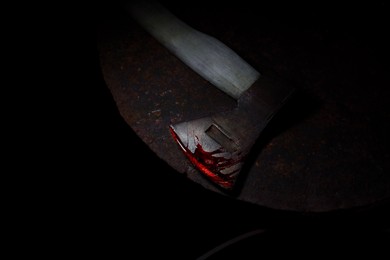 Image of Axe with blood on rusty metal surface in darkness, above view