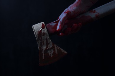 Image of Man holding bloody axe in darkness, closeup