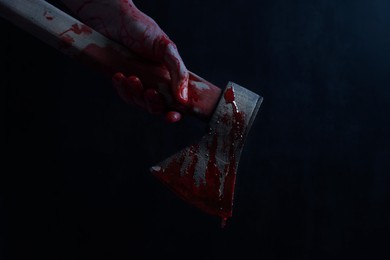 Image of Man holding bloody axe in darkness, closeup