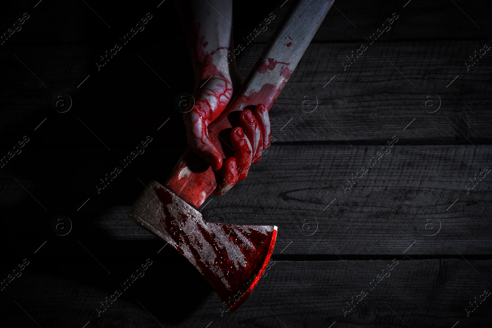 Image of Man holding bloody axe on wooden surface in darkness, top view