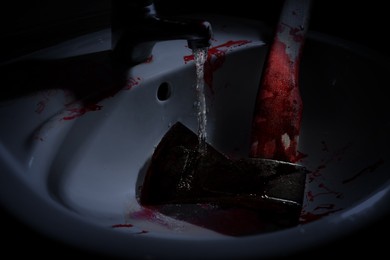 Image of Axe with blood under tap water in sink, closeup