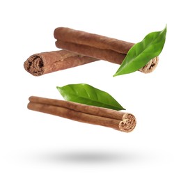 Image of Cinnamon sticks and green leaves in air on white background