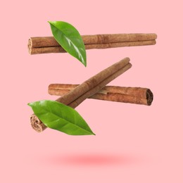 Image of Cinnamon sticks and green leaves in air on pink background