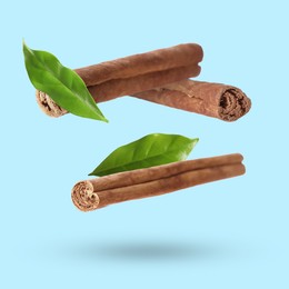 Image of Cinnamon sticks and green leaves in air on light blue background