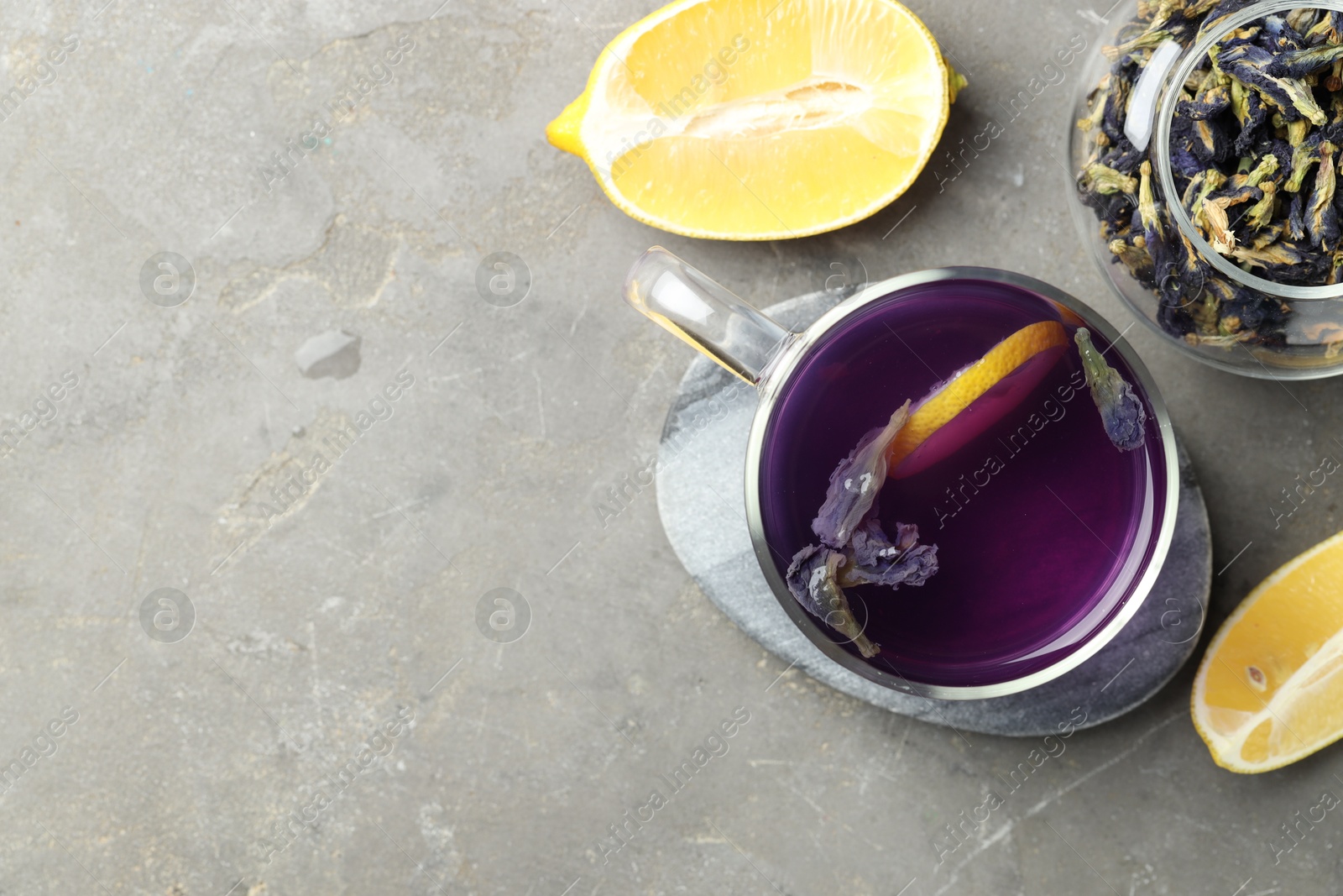 Photo of Delicious butterfly pea flower tea with lemon on gray textured table, flat lay. Space for text