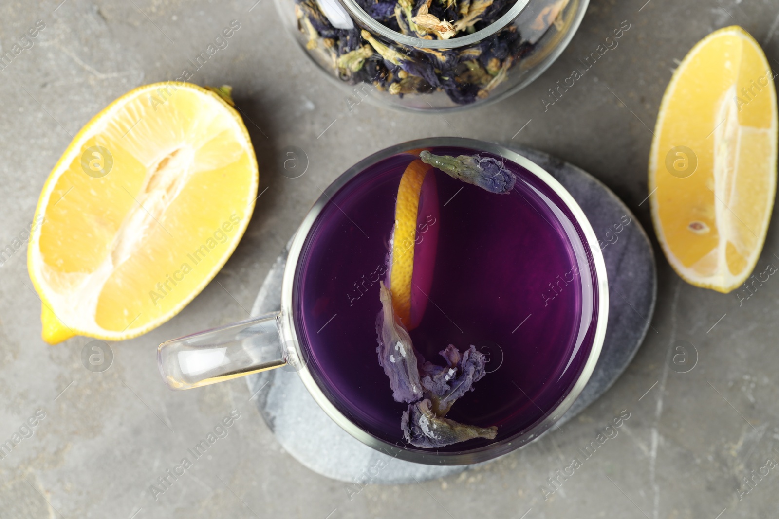 Photo of Delicious butterfly pea flower tea with lemon on gray textured table, flat lay