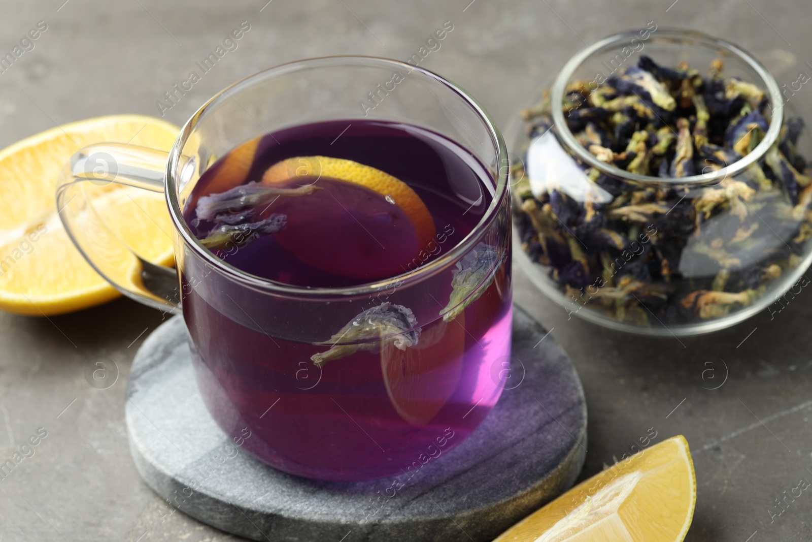 Photo of Delicious butterfly pea flower tea with lemon on gray textured table, closeup