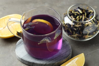 Photo of Delicious butterfly pea flower tea with lemon on gray textured table, closeup