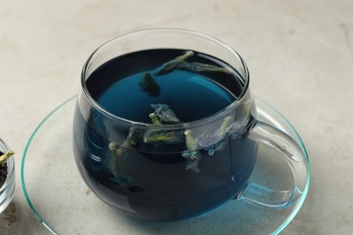 Photo of Delicious butterfly pea flower tea in cup on gray textured table, closeup