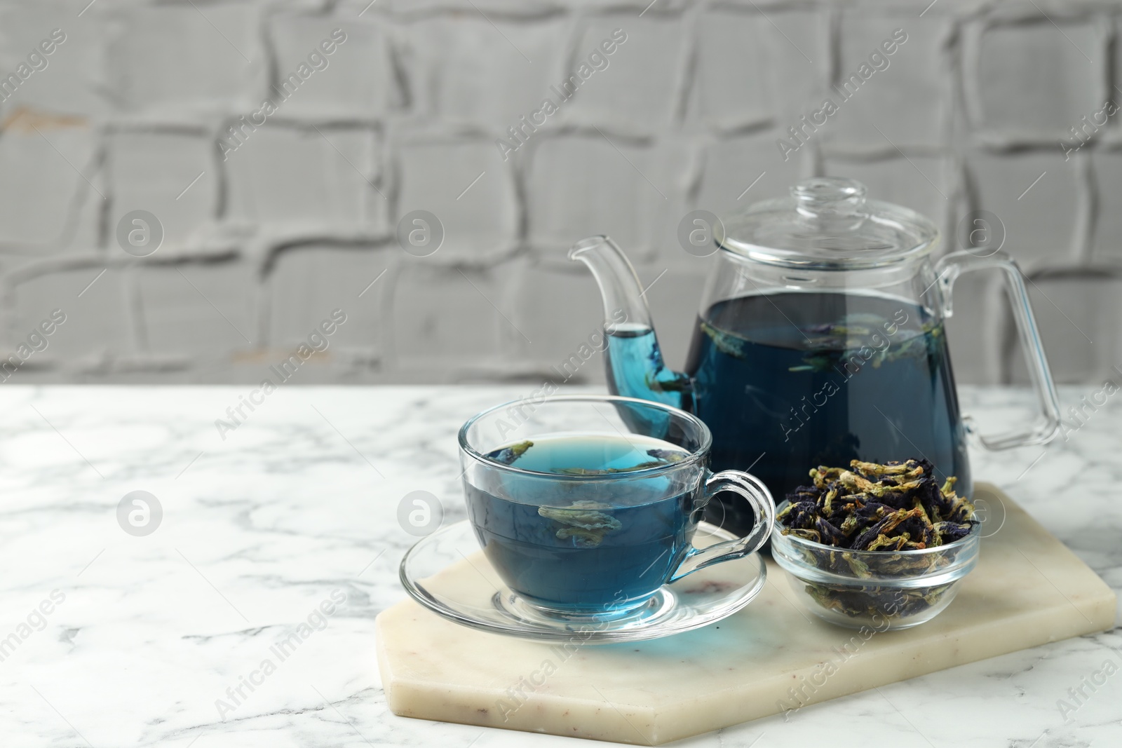 Photo of Delicious butterfly pea flower tea on white marble table against light background, space for text