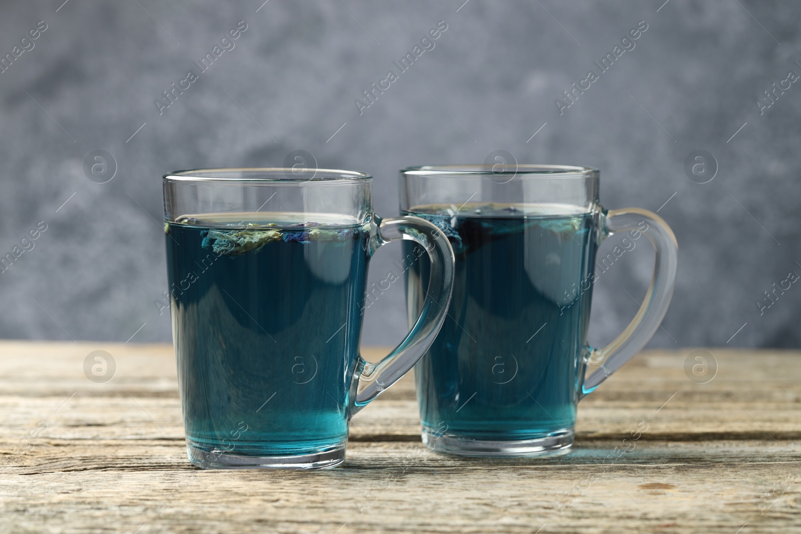 Photo of Delicious butterfly pea flower tea in cups on wooden table against gray background