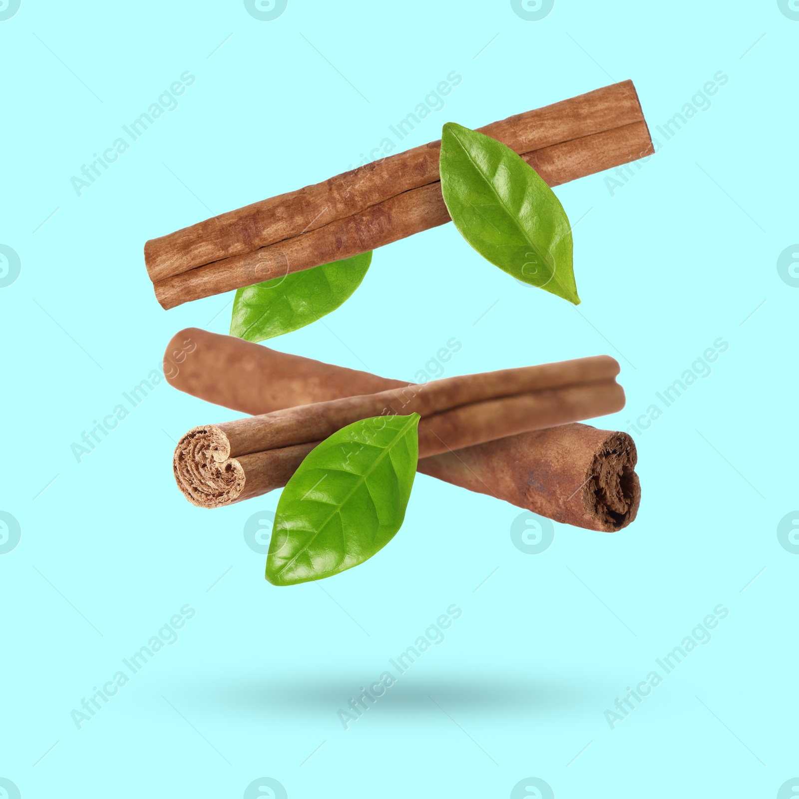 Image of Cinnamon sticks and green leaves in air on light blue background