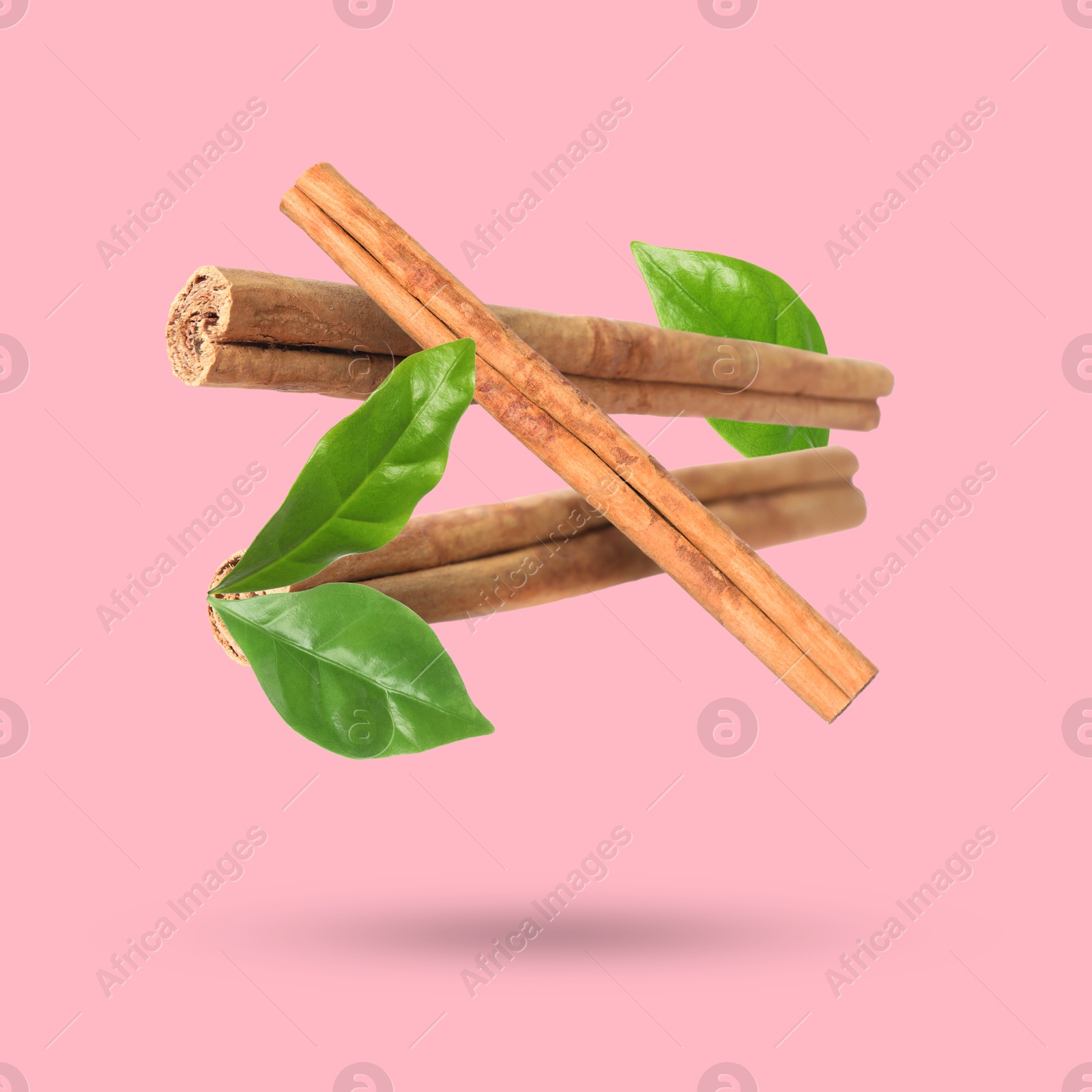 Image of Cinnamon sticks and green leaves in air on pink background