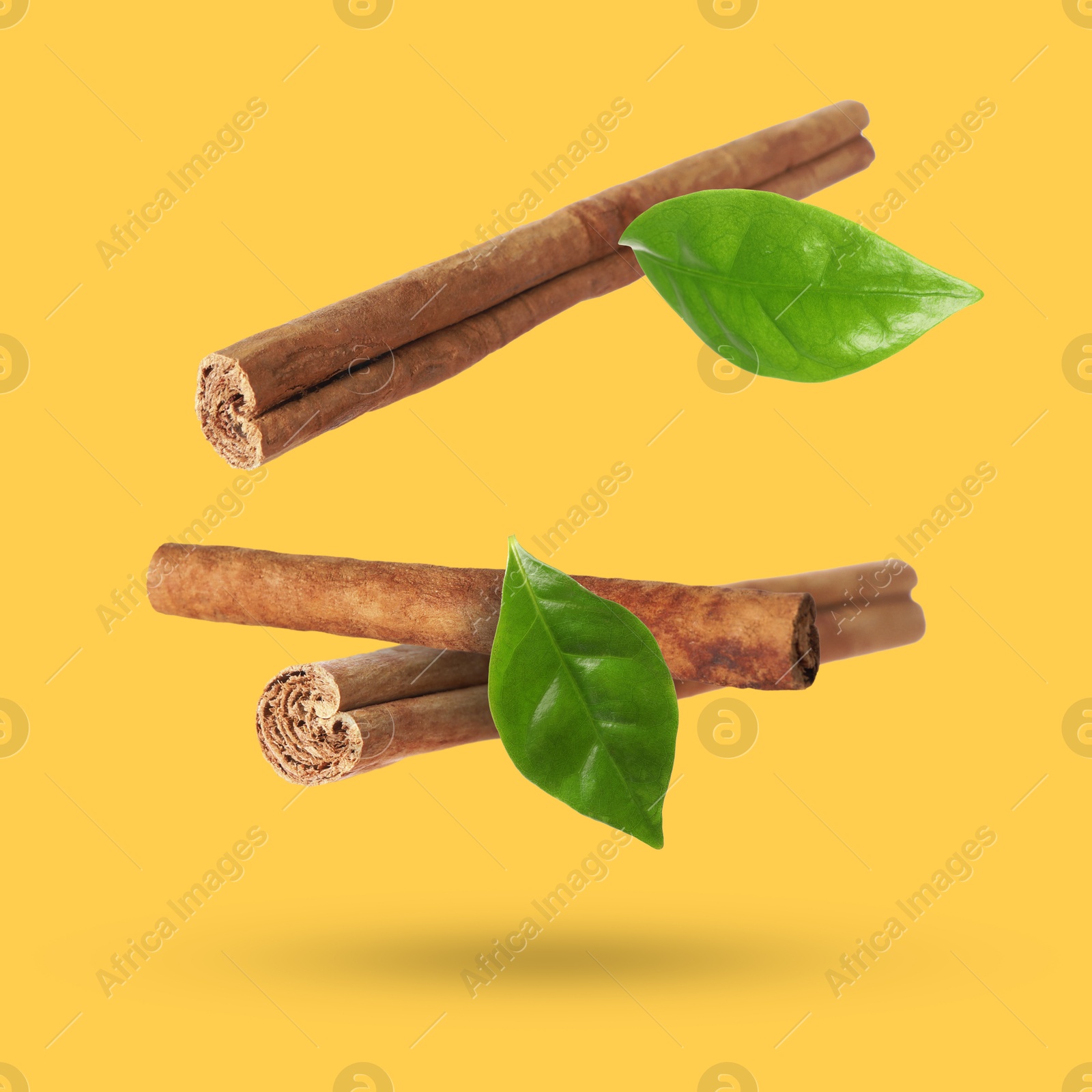 Image of Cinnamon sticks and green leaves in air on orange background