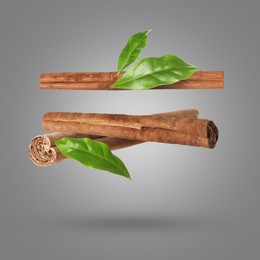 Image of Cinnamon sticks and green leaves in air on grey background