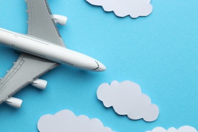 Photo of Plane model flying among paper clouds on light blue background, flat lay. Space for text