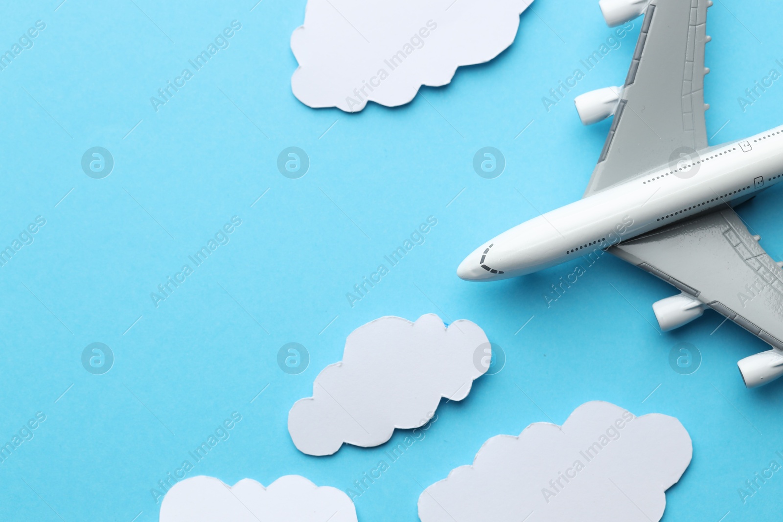 Photo of Plane model flying among paper clouds on light blue background, flat lay. Space for text