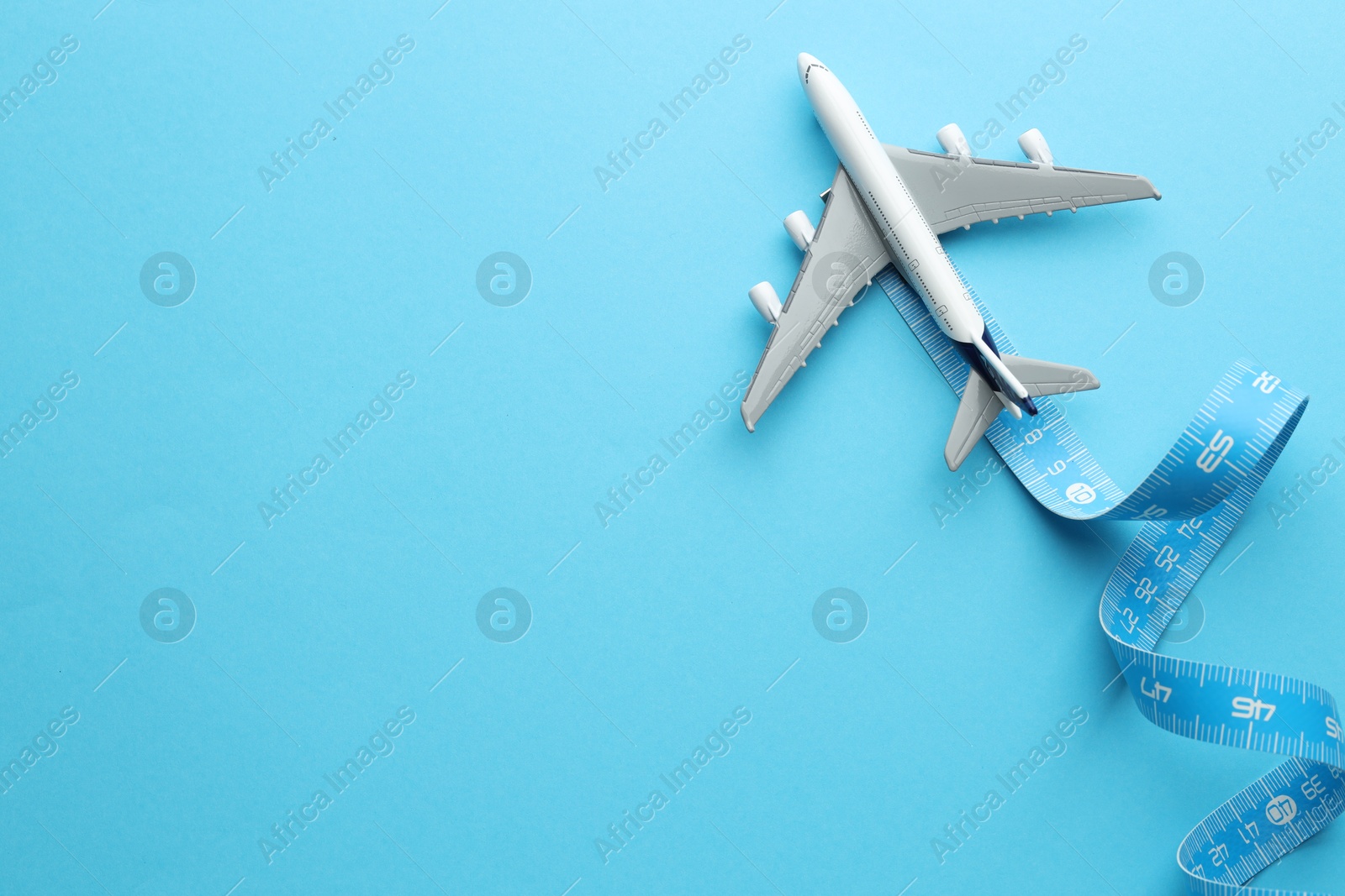 Photo of Plane model takes off and measuring tape as condensation trail on light blue background, top view. Space for text