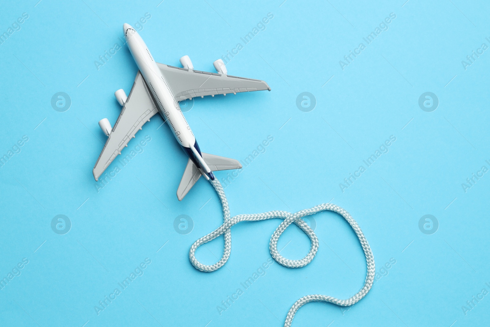 Photo of Plane model takes off and rope as condensation trail on light blue background, top view