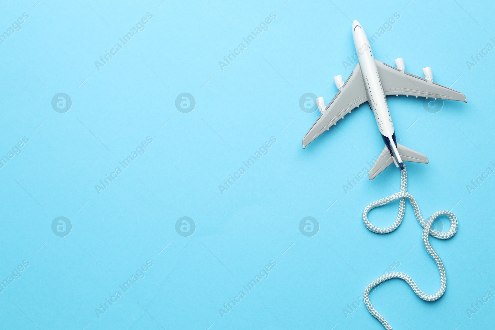 Photo of Plane model takes off and rope as condensation trail on light blue background, top view. Space for text