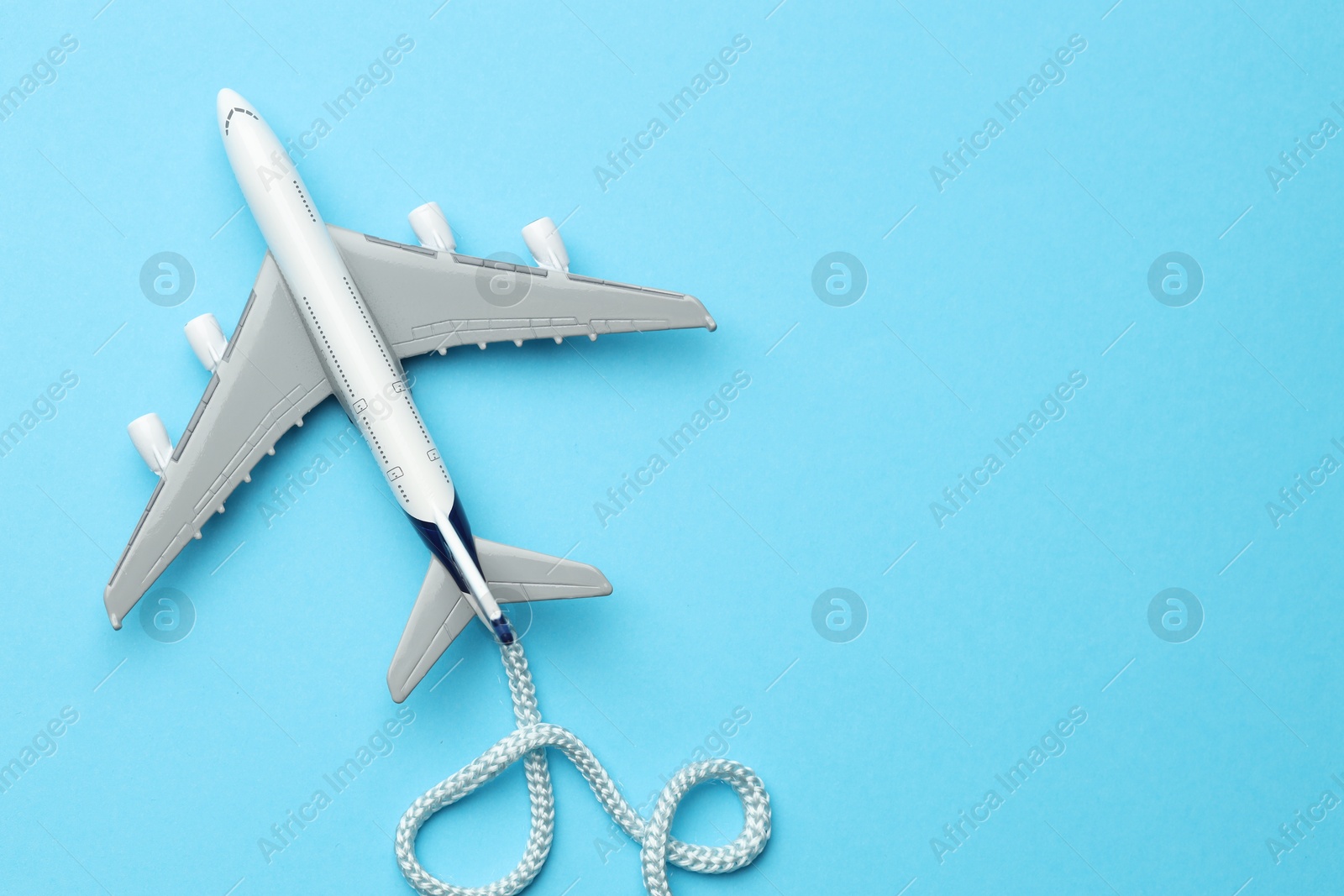 Photo of Plane model takes off and rope as condensation trail on light blue background, top view. Space for text