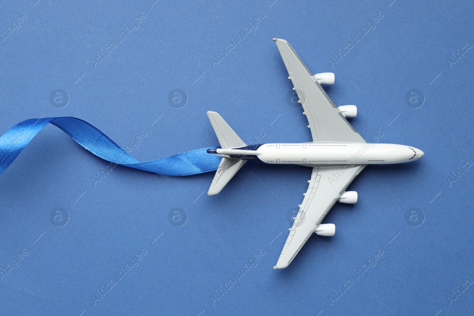 Photo of Plane model takes off and ribbon as condensation trail on blue background, top view