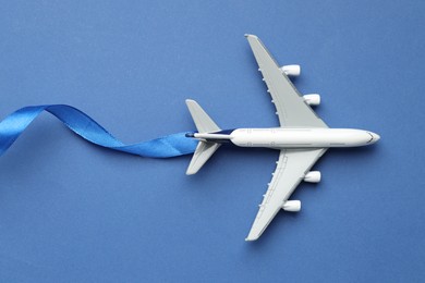 Photo of Plane model takes off and ribbon as condensation trail on blue background, top view