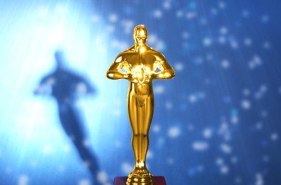 Image of Golden trophy in shape of human figure in light ray against blue shimmering background