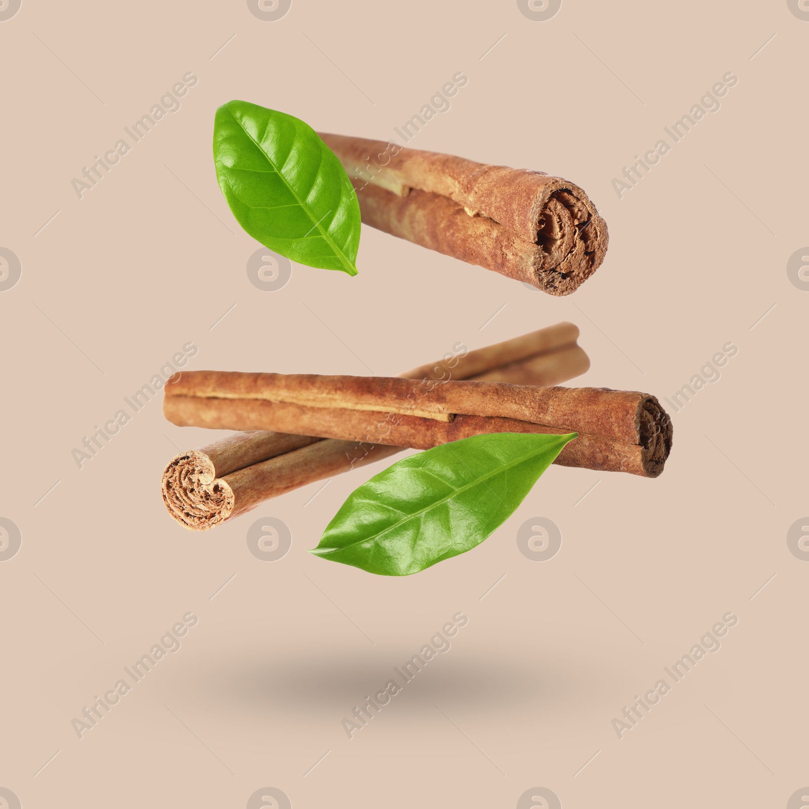 Image of Cinnamon sticks and green leaves in air on dark beige background