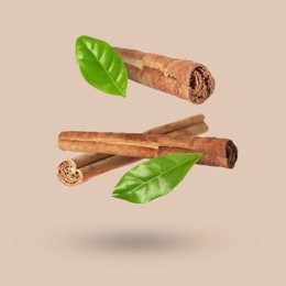 Image of Cinnamon sticks and green leaves in air on dark beige background