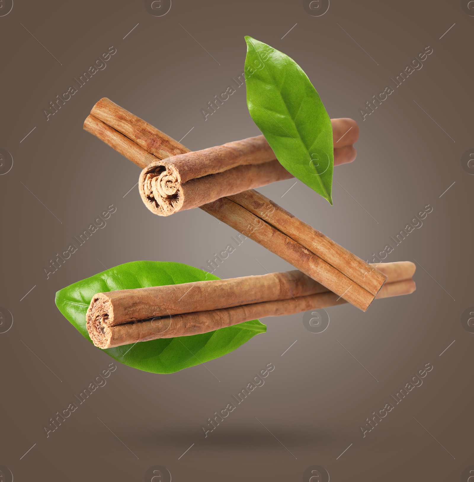 Image of Cinnamon sticks and green leaves in air on greyish brown background