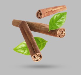 Image of Cinnamon sticks and green leaves in air on grey background