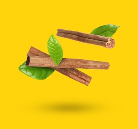 Image of Cinnamon sticks and green leaves in air on golden background