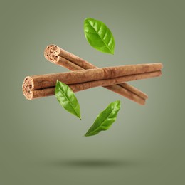 Image of Cinnamon sticks and leaves in air on greyish green background