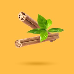 Image of Cinnamon sticks and green leaves in air on orange background