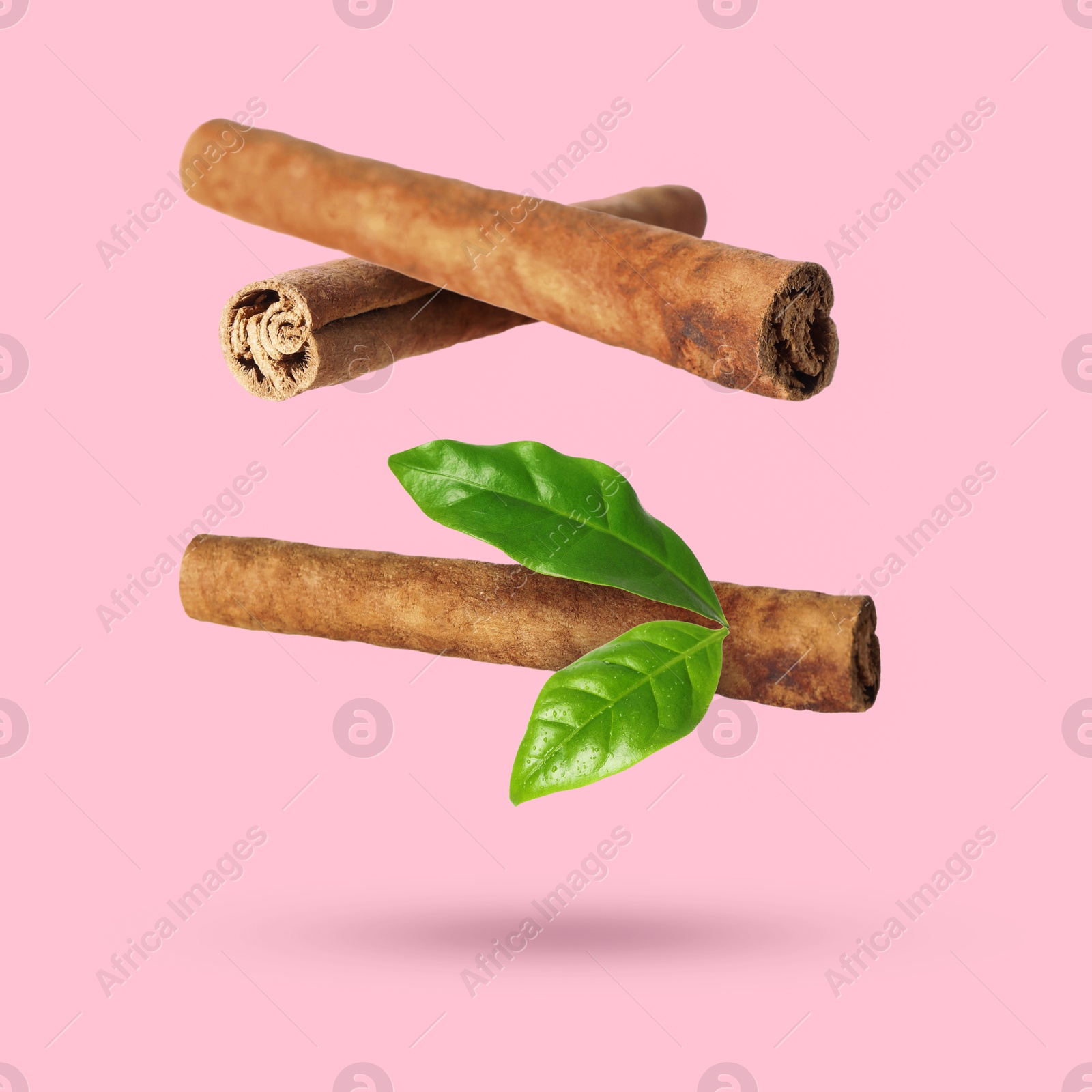 Image of Cinnamon sticks and green leaves in air on pink background