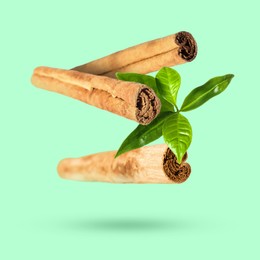 Image of Cinnamon sticks and green leaves in air on turquoise background