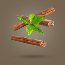 Image of Cinnamon sticks and green leaves in air on greyish brown background