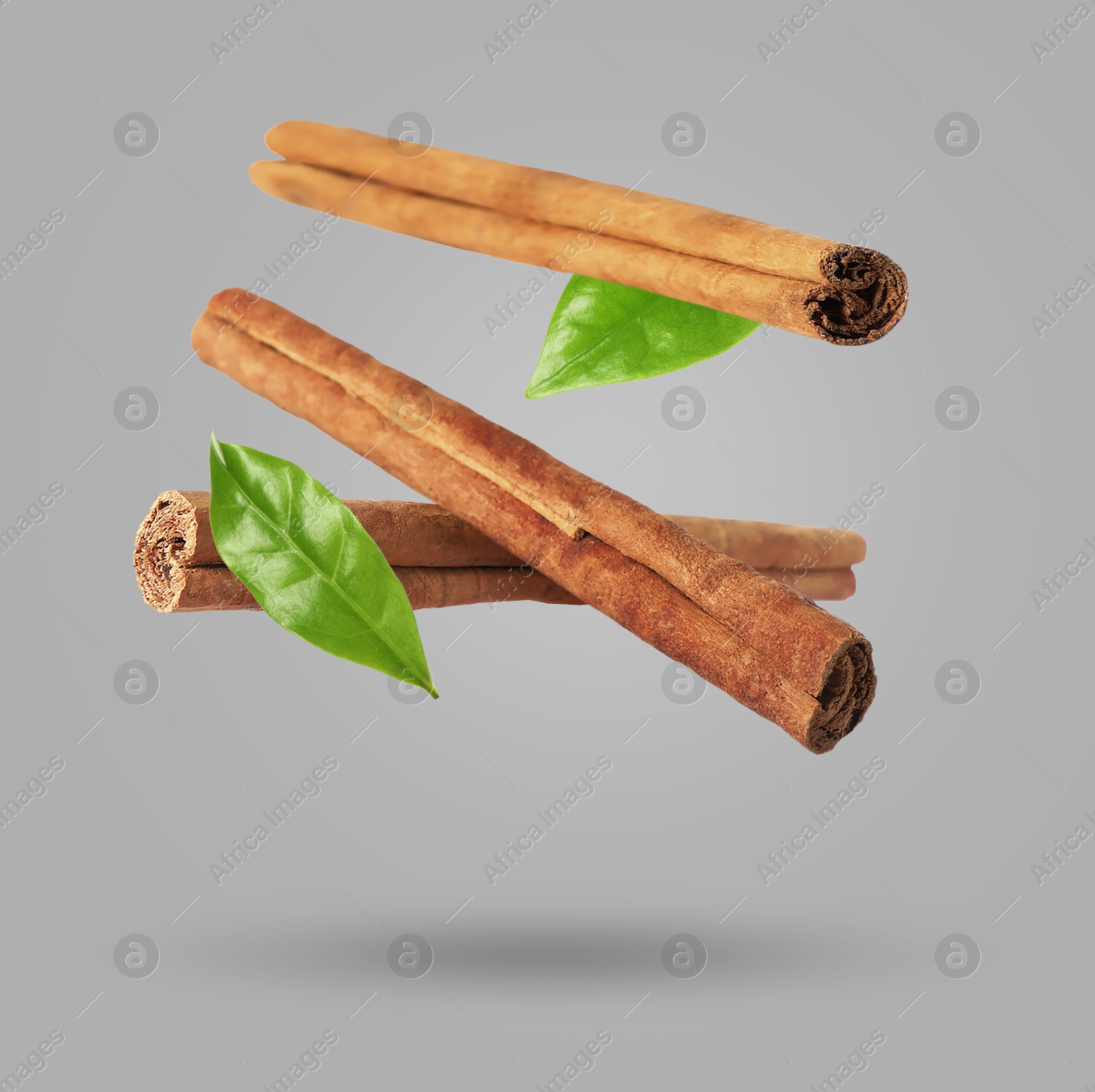 Image of Cinnamon sticks and green leaves in air on grey background