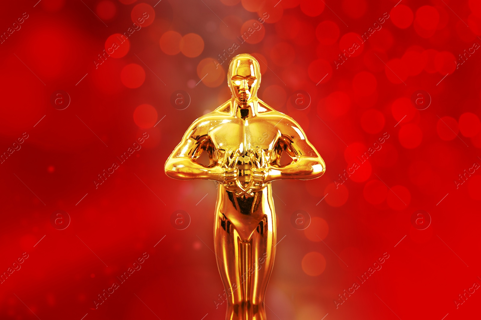 Image of Golden trophy in shape of human figure against red background with blurred lights