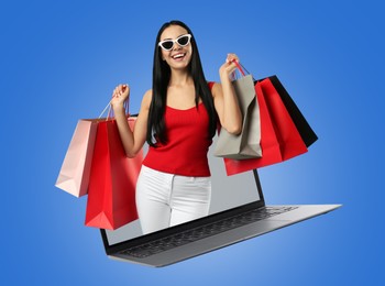 Internet shopping. Happy woman with shopping bags coming out of laptop on blue background