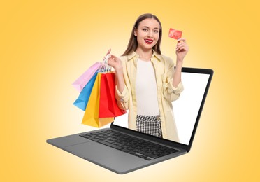 Image of Internet shopping. Happy woman with credit card and shopping bags coming out of laptop on orange background